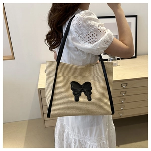 Detail of a straw tote bag featuring a black leather bow and premium woven texture