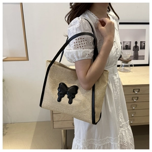 Close-up of woven straw tote bag featuring a black leather bow and long shoulder straps