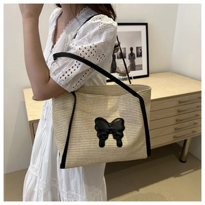 Close-up of straw tote bag with black leather butterfly appliqué and shoulder straps