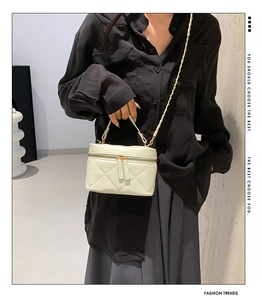 Detail of cream quilted vanity bag with gold chain strap worn by a fashion model