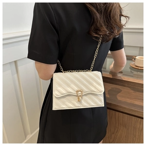 Detailed view of white quilted chain bag with gold horseshoe buckle worn by a model