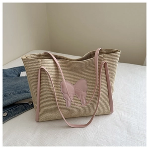 Detail of straw woven tote bag featuring a pink leather butterfly and shoulder strap