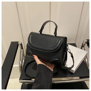 Detail einer minimalistischen schwarzen Lederhandtasche mit feinem Riemen und Logo-Prägung