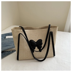 Detail view of woven straw tote bag featuring a large black butterfly patch and leather straps