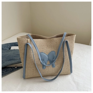 Detail of a beige straw tote bag featuring blue leather handles and a bow embellishment