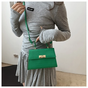 Detail of green crocodile embossed handbag featuring a gold metallic twist lock closure
