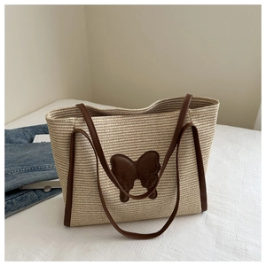 Detail of straw tote bag with brown leather butterfly patch on a white background