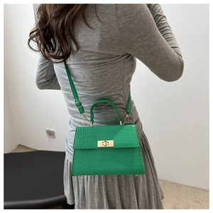 Detail of green crocodile texture leather bag with gold twist lock on model in grey dress
