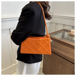Detailed view of orange quilted leather underarm bag with knot strap and metal accents