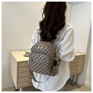 Detail view of khaki checkered backpack with brown leather trim and metallic zippers