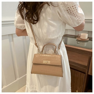 Detail of beige crocodile pattern handbag with gold hardware shown on person's shoulder