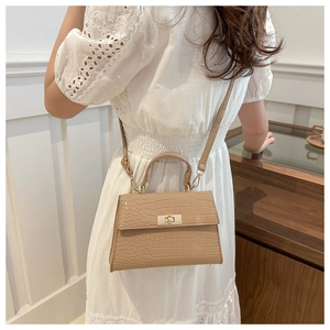Close-up of beige crocodile pattern handbag showing metal lock and adjustable strap