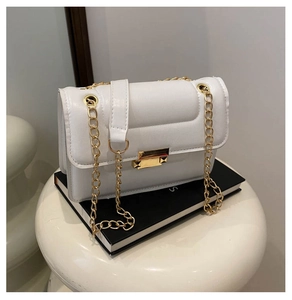 Close-up of minimalist white leather flap bag with gold chain strap and metal lock