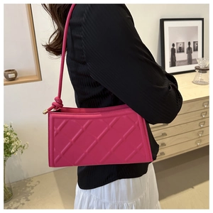 Detail of rose red quilted shoulder bag with unique knotted strap on a model