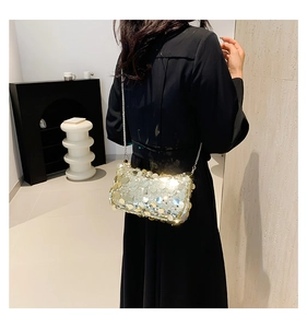 Detail of a gold sequin handbag with chain strap against a black dress for party wear