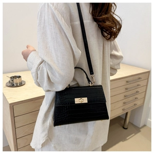 Side view of black crocodile pattern handbag with gold clasp on a minimalist background