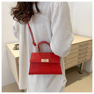 Detail view of red crocodile textured crossbody bag with gold lock and metal feet
