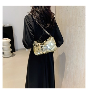 Detail of a gold sequin crossbody bag with a silver chain strap worn on a black dress