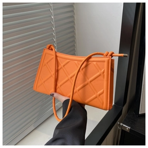 Détail d'un sac à bandoulière matelassé orange vif avec motif losanges 3D et embouts métal
