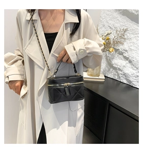 Detail of black quilted box bag with gold chain strap and top handle on trench coat