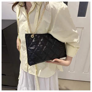 Close-up of a black quilted tote bag with gold chain strap on a model shoulder