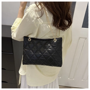 Detail of black quilted tote bag with gold chain strap worn by model in home setting