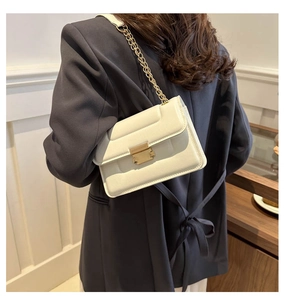 Minimalist white leather crossbody bag with gold chain strap and metallic lock on suit