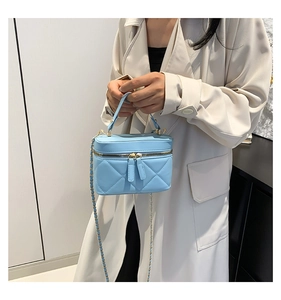 Close-up of sky blue quilted crossbody bag with gold chain and dual zipper details