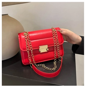 Detail of red quilted shoulder bag with gold hardware and chain strap on black table