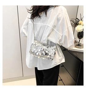 Detail of silver sequin handbag with chain strap shown on model in a modern interior