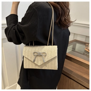 Détail du sac bandoulière en paille beige avec nœud en strass et chaîne dorée