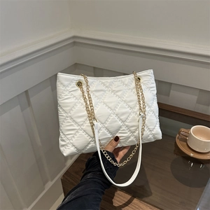 White quilted tote bag with gold chain strap shown in a minimalist modern lifestyle setting
