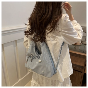 Detail of light blue hobo bag with pearls, diamond bow, and woven chain strap on shoulder