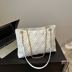 White quilted tote bag with gold chain strap placed on a desk for office commute