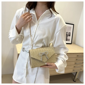 Détail du sac bandoulière en paille tissée avec nœud déco et chaîne dorée