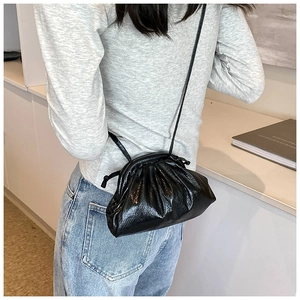 Detail view of a black glossy pleated dumpling bag with thin shoulder strap on a model