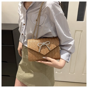 Sac bandoulière en paille tressée marron avec nœud en strass porté par un mannequin