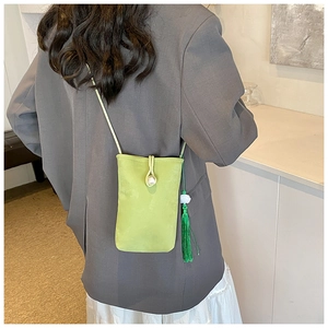 Detail of green mini crossbody bag with pearl closure and fringe tassel on grey coat