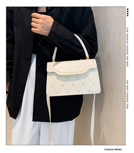 Close-up of white quilted handbag with golden heart studs and embroidery detail