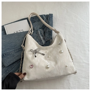 Detailed view of silver bow charm and white pearls on pleated white bucket bag