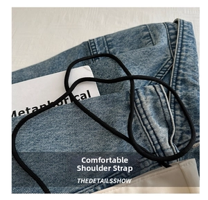 Detail van de dunne zwarte trekkoordriem op blauwe denim en beige geweven stof