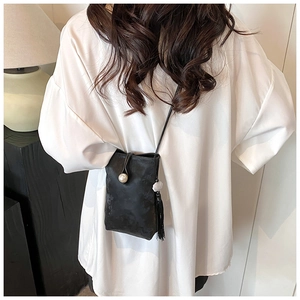 Dettaglio borsa a tracolla nera vintage con chiusura a perla e frange su camicia bianca