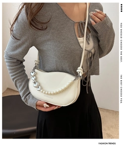 Detail of white crescent shoulder bag featuring pearl and silver heart chain accessories