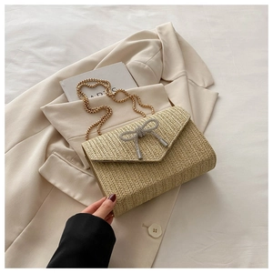 Vue détaillée du sac enveloppe en paille beige avec un nœud en strass étincelant