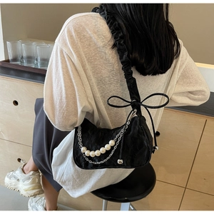 Detail of black pleated half-moon bag with pearl chain and bow shoulder strap accents