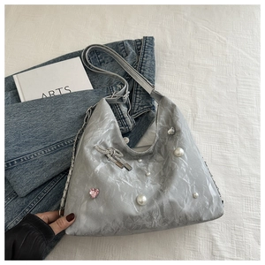 Detail of silver tote bag featuring pearl accents, a pink crystal heart, and a metal bow charm