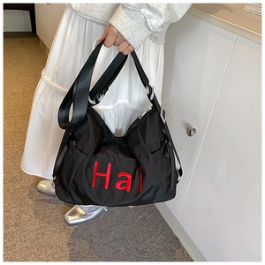 Detail of black nylon tote with red Hai embroidery and adjustable strap on model