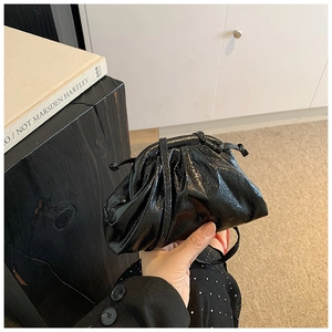 Detail of black glossy pleated shell bag with fine texture and slim strap