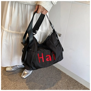 Detail of black nylon messenger bag featuring a bold red 'Hai' embroidery contrast