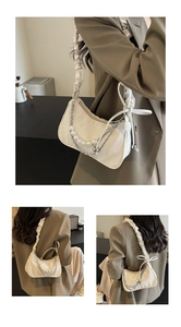 Détail de la bandoulière plissée et de la chaîne de perles sur un sac sous le bras crème